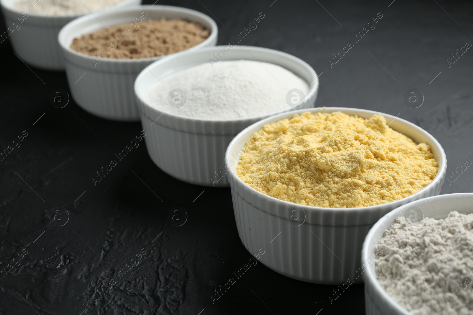 Different types of flour in bowls on black textured table, closeup Photo of Different types of flour in bowls on black textured table, closeup