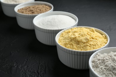 Photo of Different types of flour in bowls on black textured table, closeup