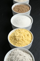 Photo of Different types of flour in bowls on black textured table, closeup