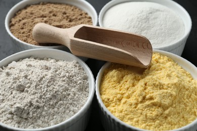 Photo of Different types of flour in bowls and scoop on table, closeup