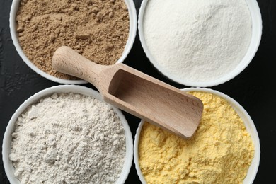 Photo of Different types of flour in bowls and scoop on table, top view