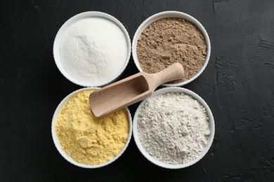 Photo of Different types of flour in bowls and scoop on black textured table, top view