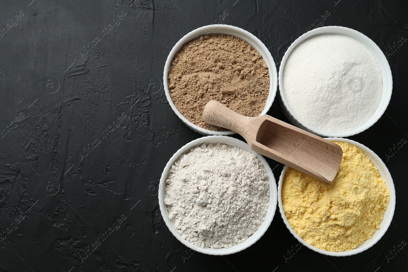 Different types of flour in bowls and scoop on black textured table, top view. Space for text Photo of Different types of flour in bowls and scoop on black textured table, top view. Space for text