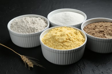 Photo of Different types of flour in bowls and spike on black textured table, closeup