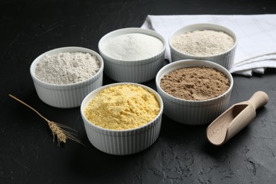 Photo of Different types of flour in bowls, scoop and spike on black textured table