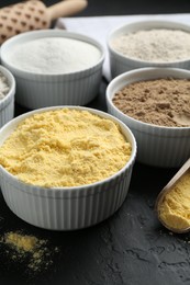 Photo of Different types of flour in bowls on black textured table, closeup