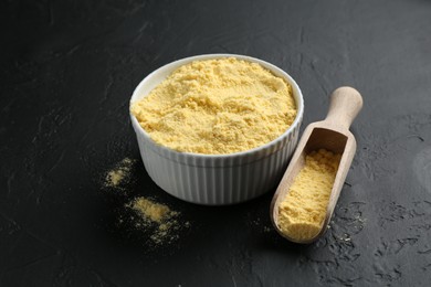 Photo of Corn flour in bowl and scoop on black textured table