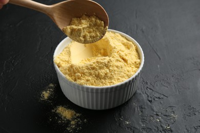 Photo of Taking corn flour with spoon from bowl on black textured table, closeup