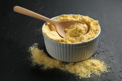 Photo of Corn flour in bowl and spoon on black textured table, closeup