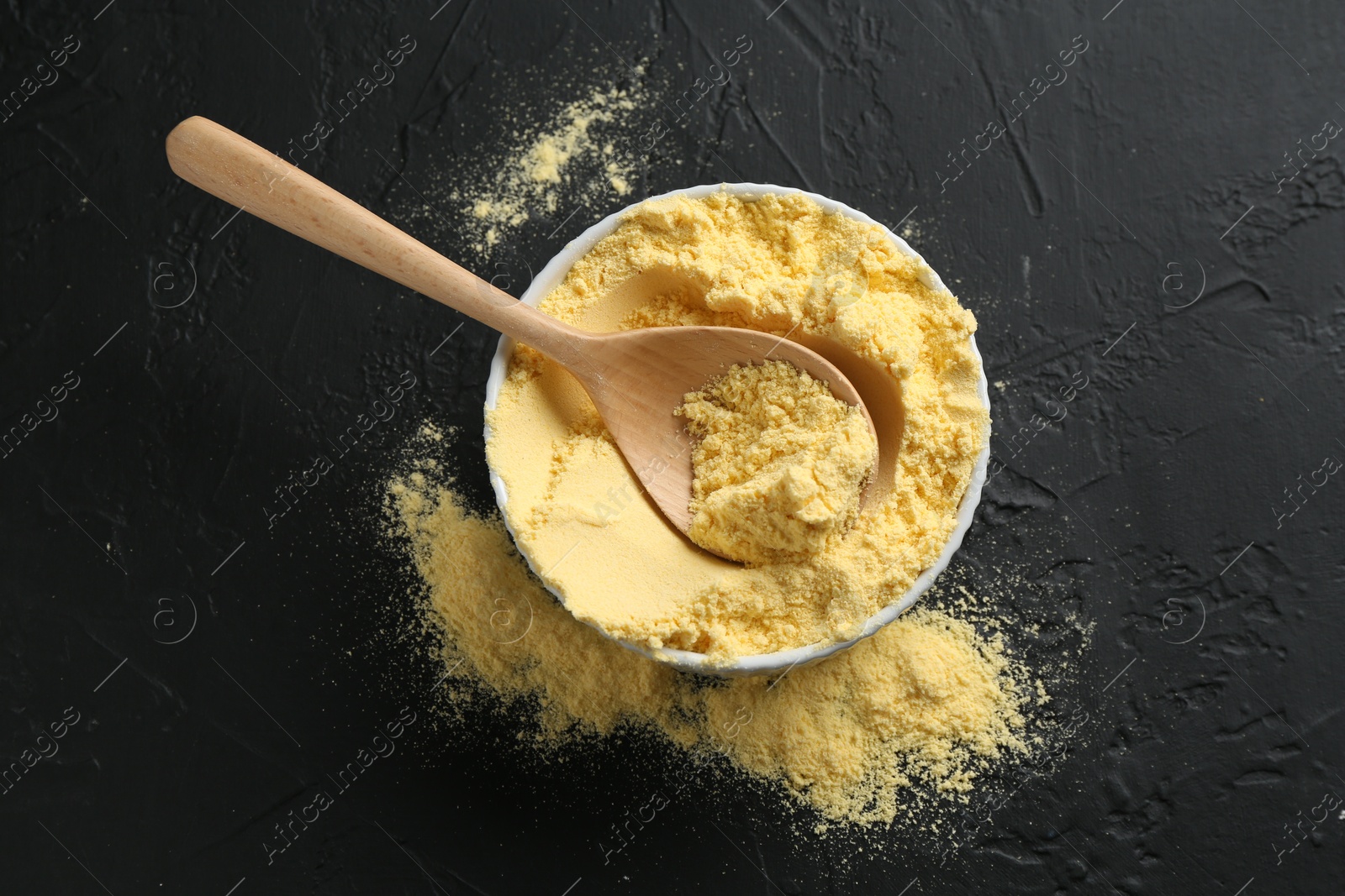 Corn flour in bowl and spoon on black textured table, top view Photo of Corn flour in bowl and spoon on black textured table, top view