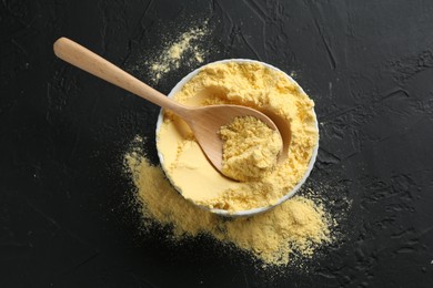 Photo of Corn flour in bowl and spoon on black textured table, top view
