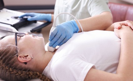 Photo of Sonographer conducting girl's thyroid gland ultrasound examination in clinic, closeup