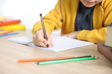 Photo of Little boy doing homework at wooden table indoors, closeup