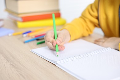 Photo of Little boy doing homework at wooden table indoors, closeup