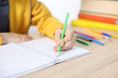 Photo of Little boy doing homework at wooden table indoors, closeup