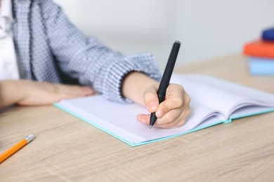 Photo of Little boy doing homework at wooden table indoors, closeup