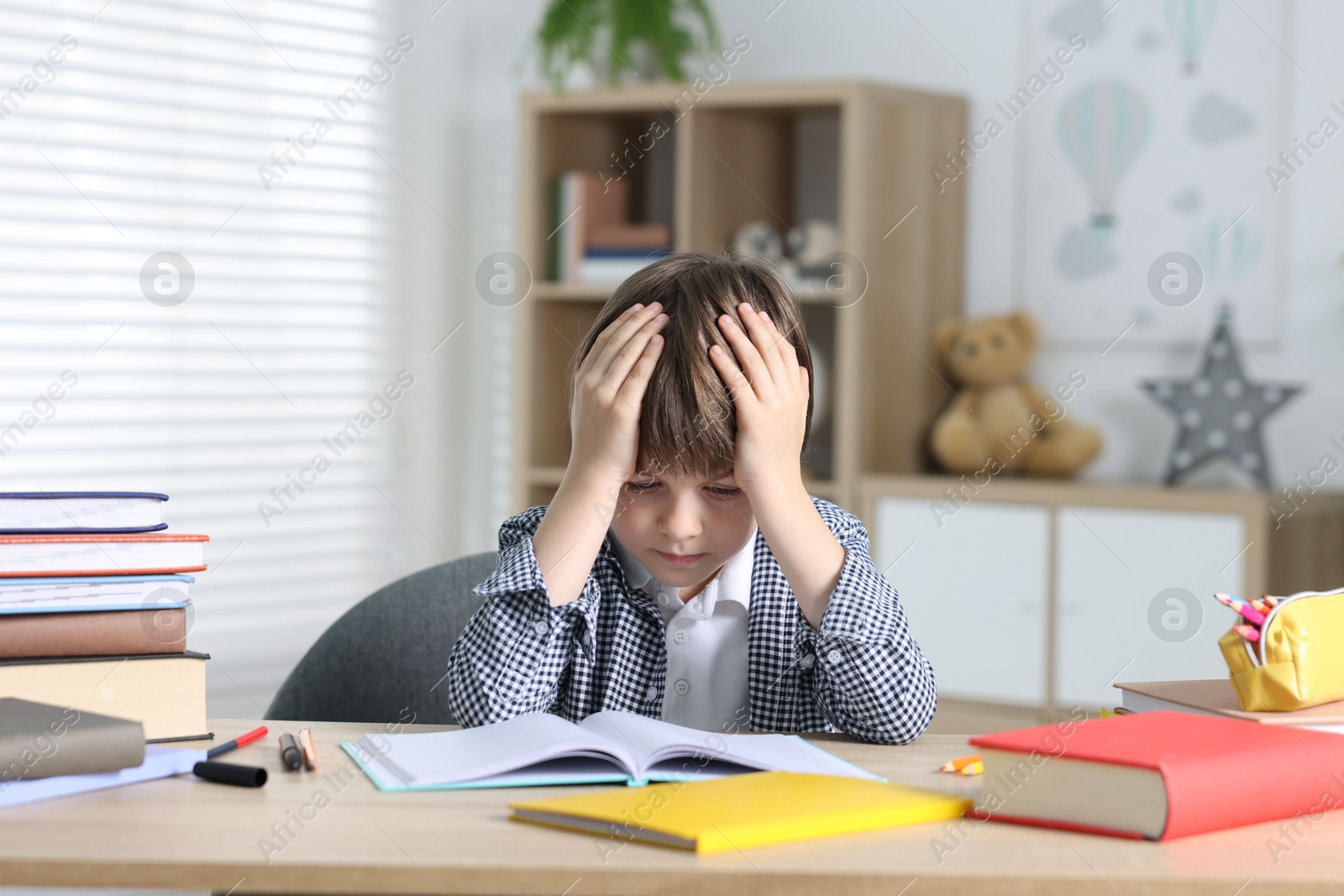 Photo of Tired little boy doing homework at table indoors