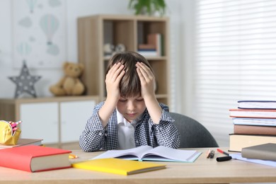 Photo of Tired little boy doing homework at table indoors