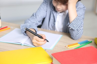 Photo of Little boy doing homework at wooden table indoors