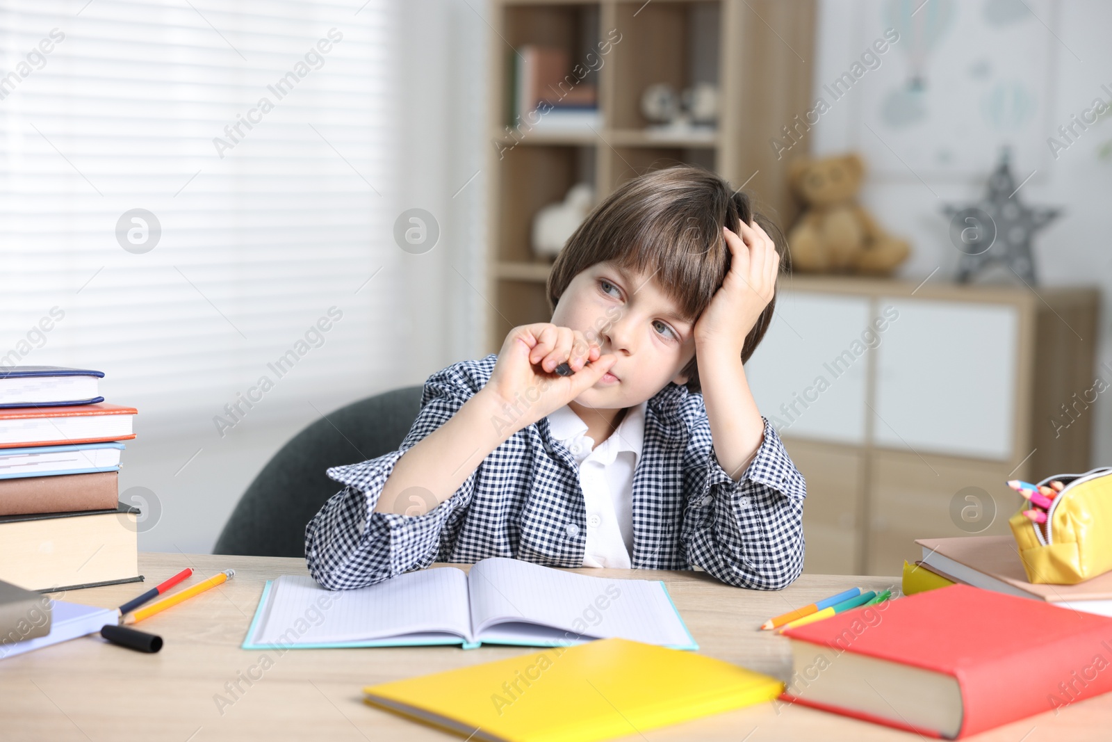 Photo of Thoughtful little boy doing homework at table indoors