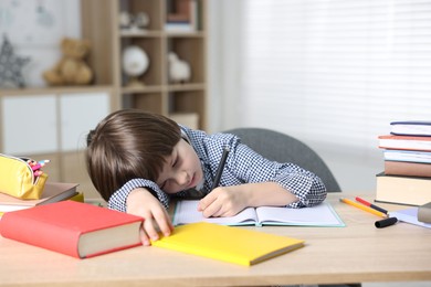 Photo of Tired little boy doing homework at table indoors