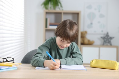 Photo of Cute little boy doing homework at table indoors