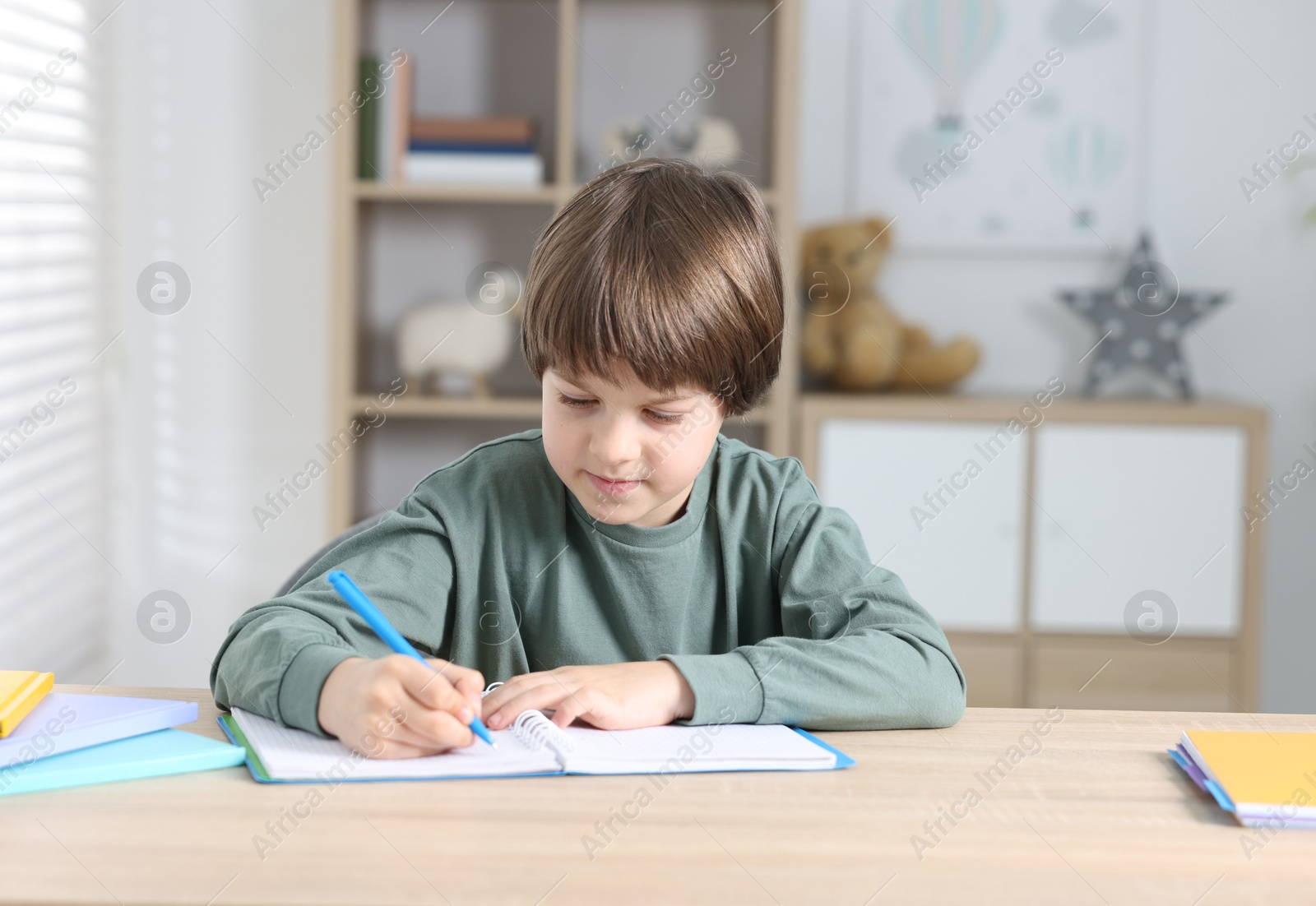 Photo of Cute little boy doing homework at table indoors