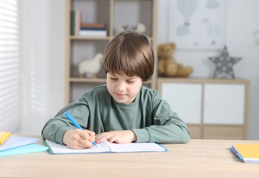 Photo of Cute little boy doing homework at table indoors