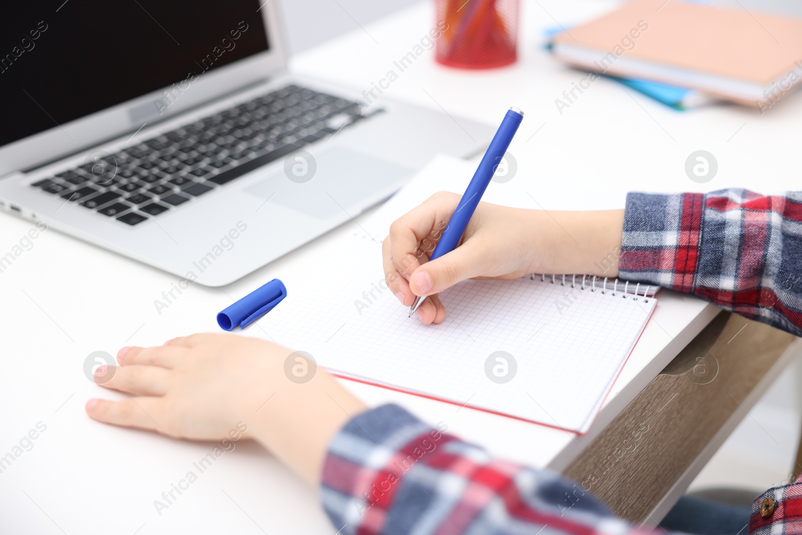 Photo of Little boy doing homework at white table indoors, closeup
