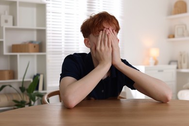 Photo of Teen problems. Depressed teenage boy at table indoors
