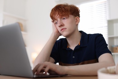 Photo of Teen problems. Depressed teenage boy with laptop at desk indoors