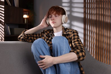 Photo of Teen problems. Depressed teenage boy listening to music on sofa at home