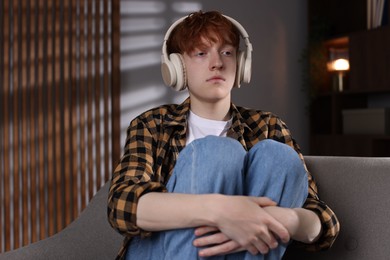 Photo of Teen problems. Depressed teenage boy listening to music on sofa at home