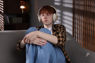 Photo of Teen problems. Depressed teenage boy listening to music on sofa at home
