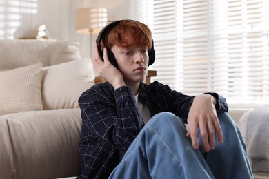 Photo of Teen problems. Depressed teenage boy listening to music on floor at home