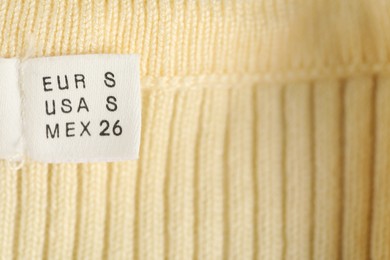 Photo of Clothing label with size on knitted garment as background, closeup