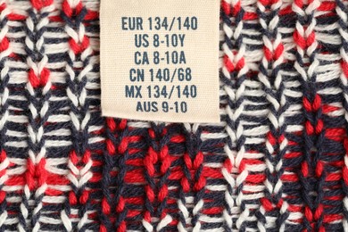 Photo of Clothing label with size on knitted garment as background, top view