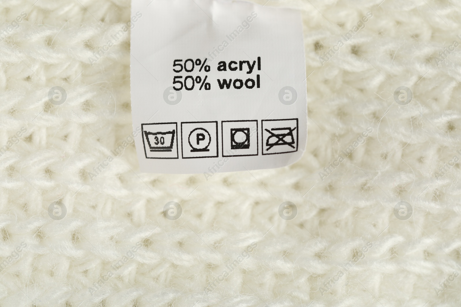 Photo of Clothing label with care symbols and material content on knitted garment as background, top view