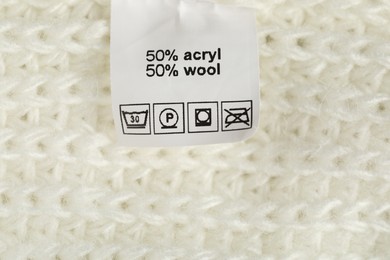 Photo of Clothing label with care symbols and material content on knitted garment as background, top view