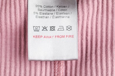 Photo of Clothing label with care symbols and material content on knitted garment as background, top view
