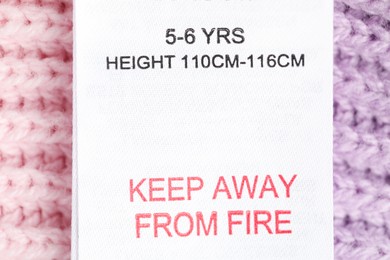 Photo of Clothing label with care advice and size on knitted garment as background, top view