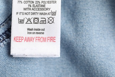 Photo of Clothing label with care symbols and material content on light blue garment as background, top view