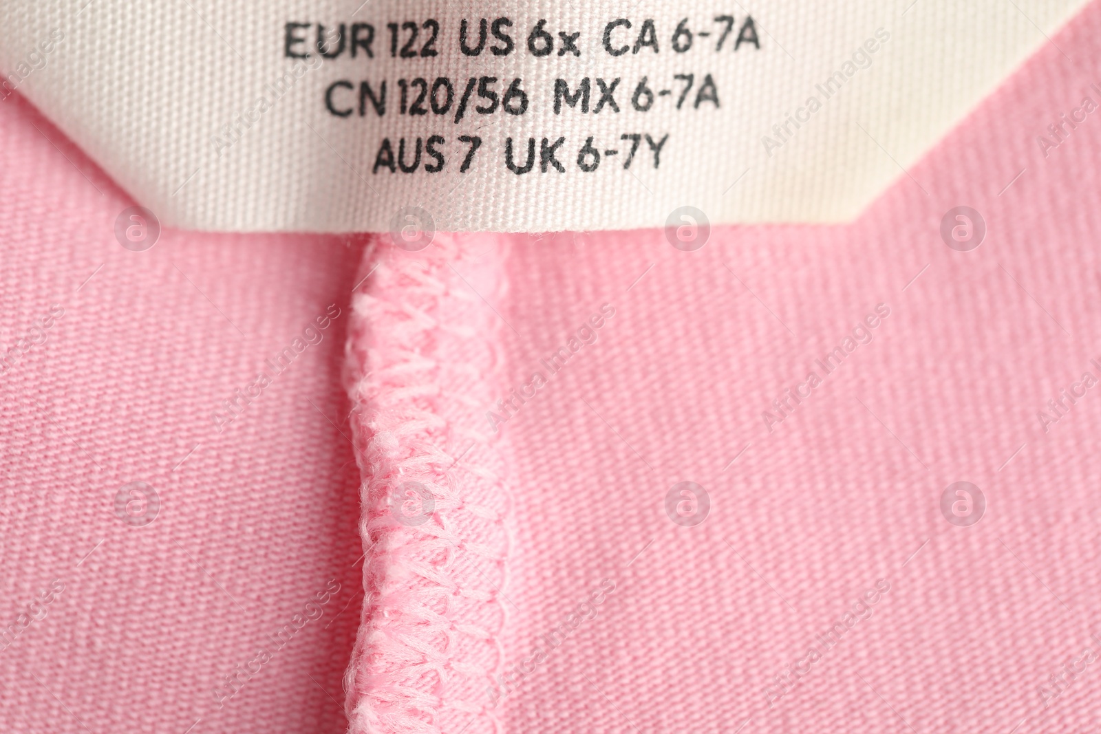 Photo of Clothing label with size on pink garment as background, closeup