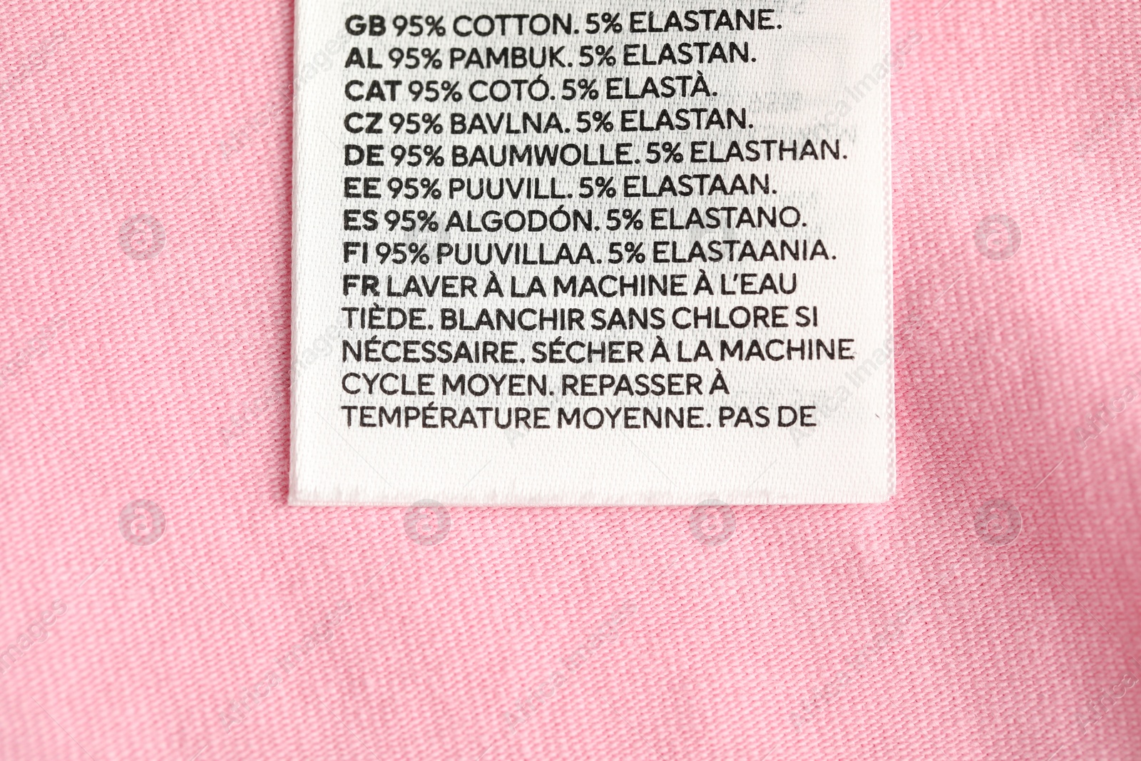 Clothing label with care advice and size on pink garment as background, top view Photo of Clothing label with care advice and size on pink garment as background, top view