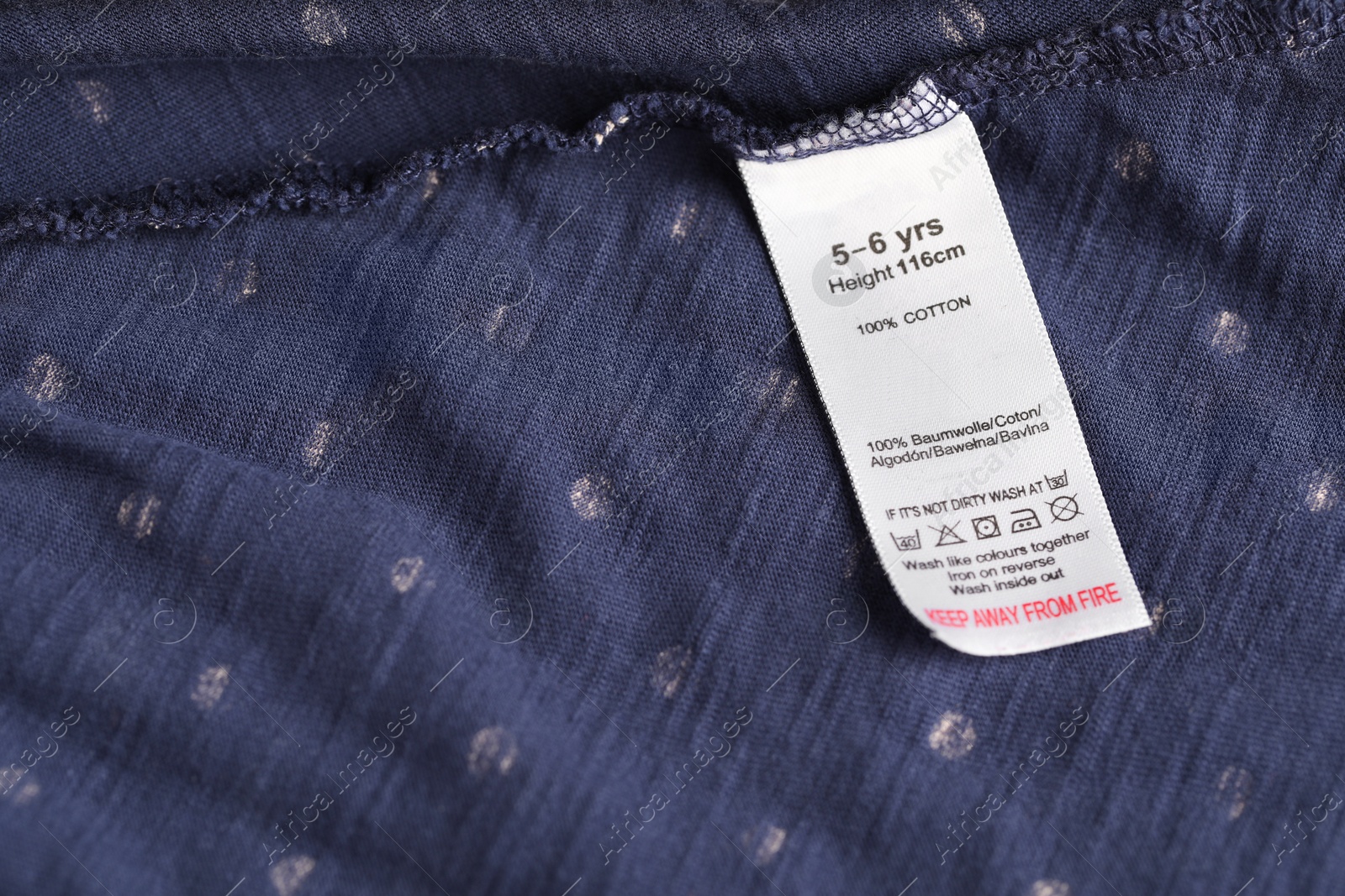Photo of Clothing label with care symbols and material content on blue garment as background, above view