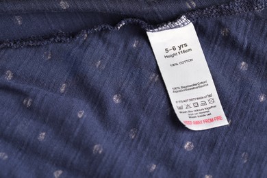 Photo of Clothing label with care symbols and material content on blue garment as background, above view