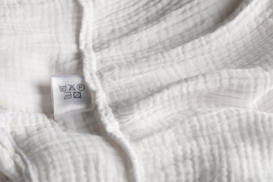 Photo of Clothing label with care symbols on white garment as background, closeup