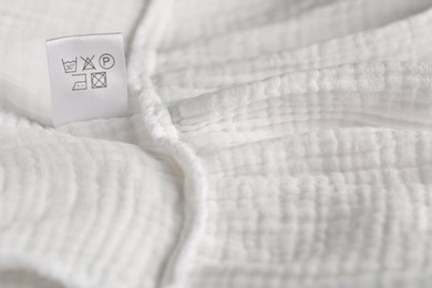 Photo of Clothing label with care symbols on white garment as background, closeup