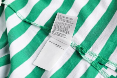 Photo of Clothing label on striped garment as background, closeup