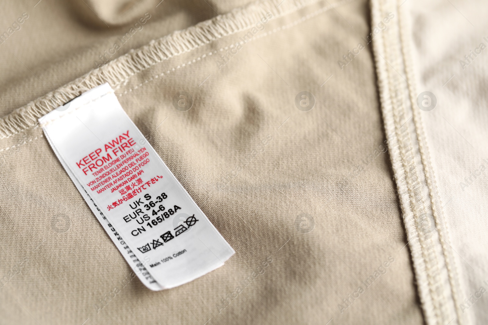 Photo of Clothing label with care symbols and size on beige garment as background, closeup